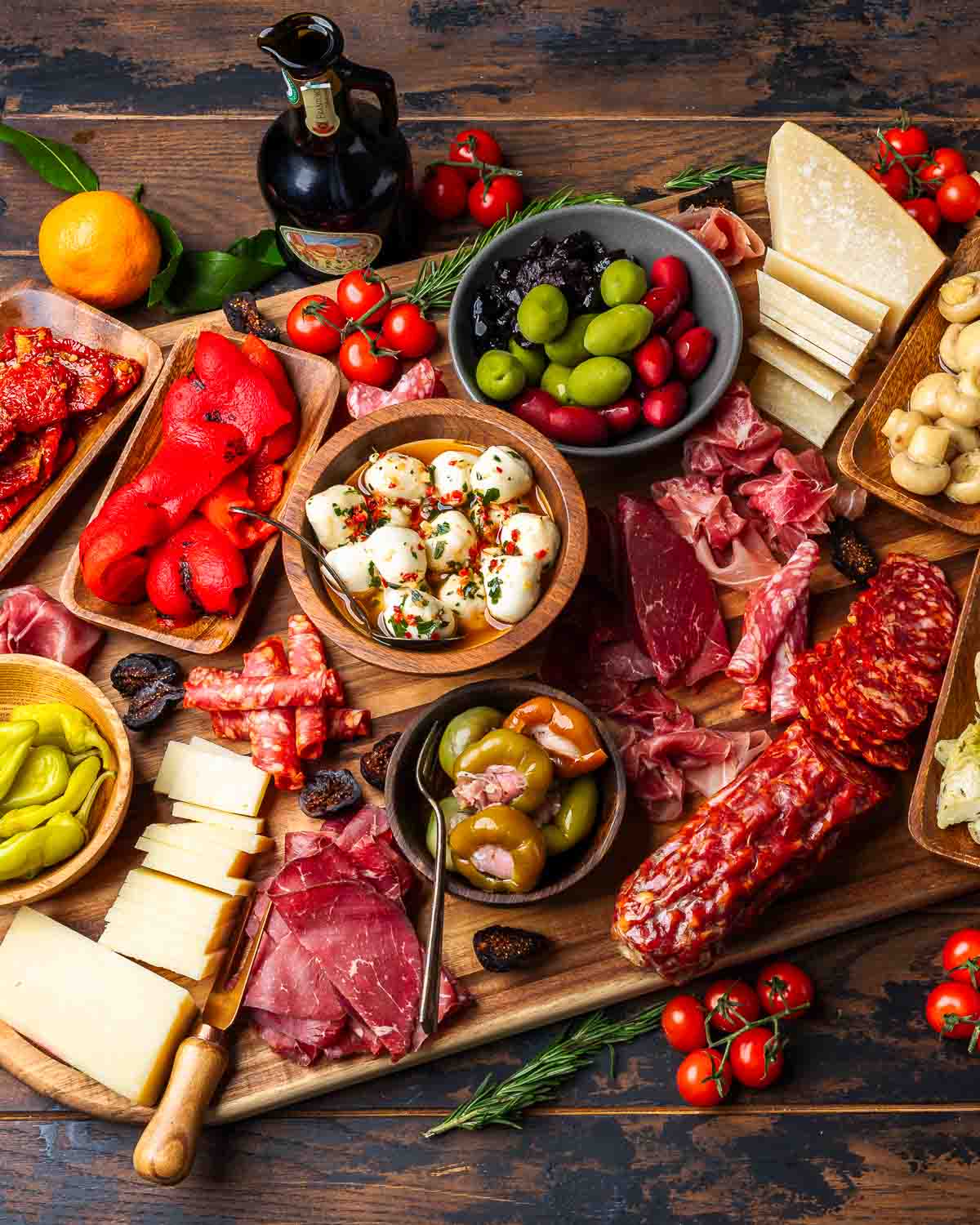 Appetizer board with cured meats, cheeses, pickled vegetables, figs, and olive oil.