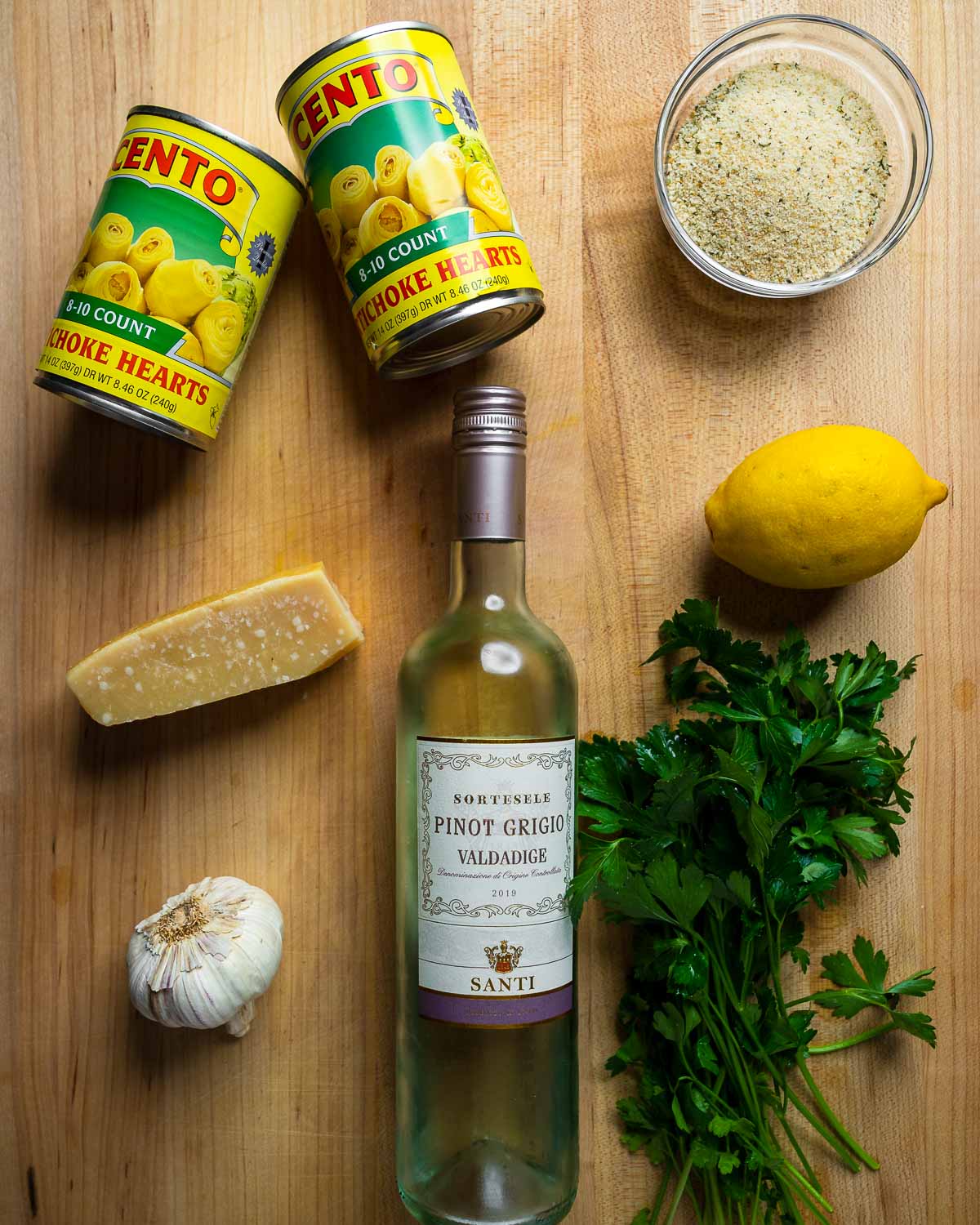 Ingredients shown: canned artichoke hearts, breadcrumbs, parmesan block, lemon, wine, garlic, and parsley.