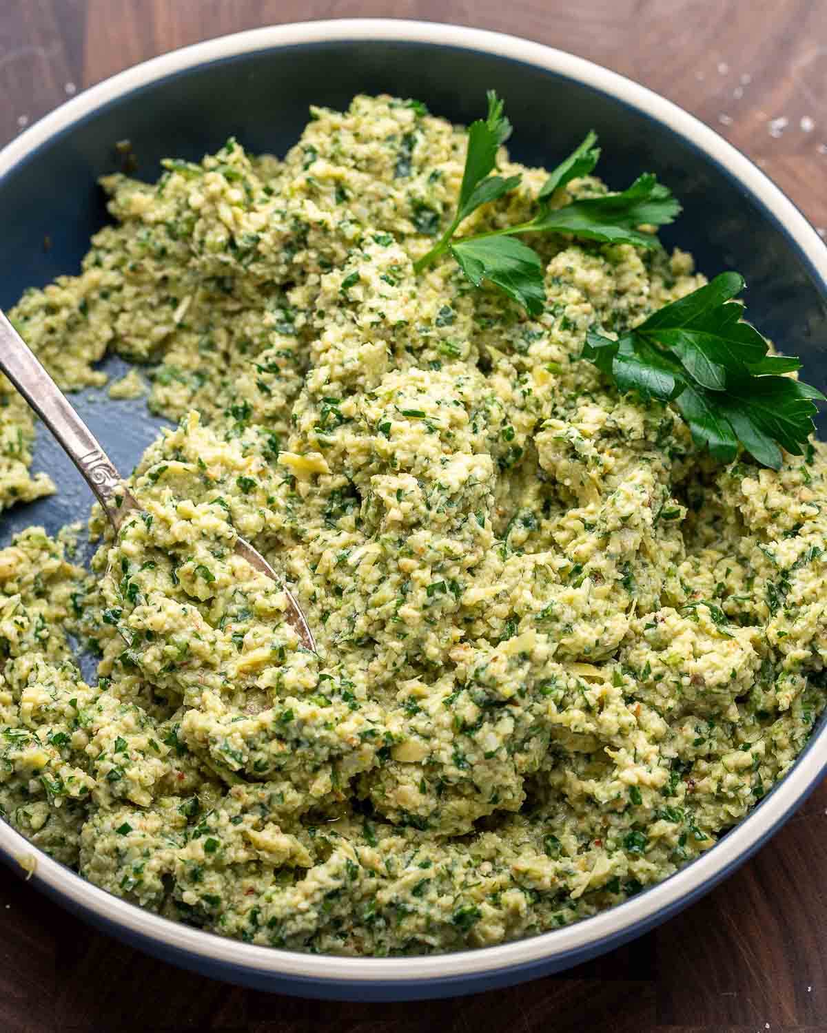 Artichoke pesto in blue bowl on walnut board.