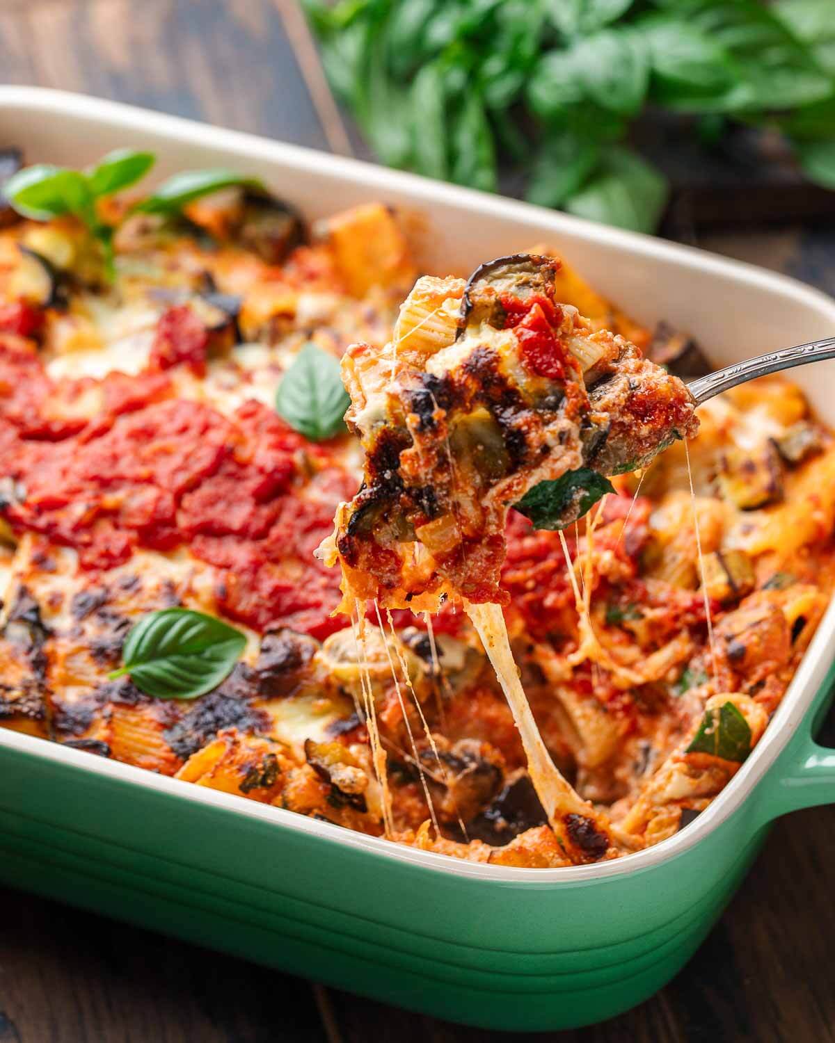 Serving spoon pulling scoop of baked eggplant pasta out of baking dish.