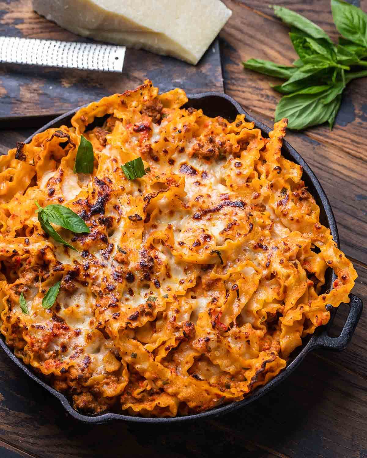 Baked lasagna pie on wood board with basil and Pecorino in the background.