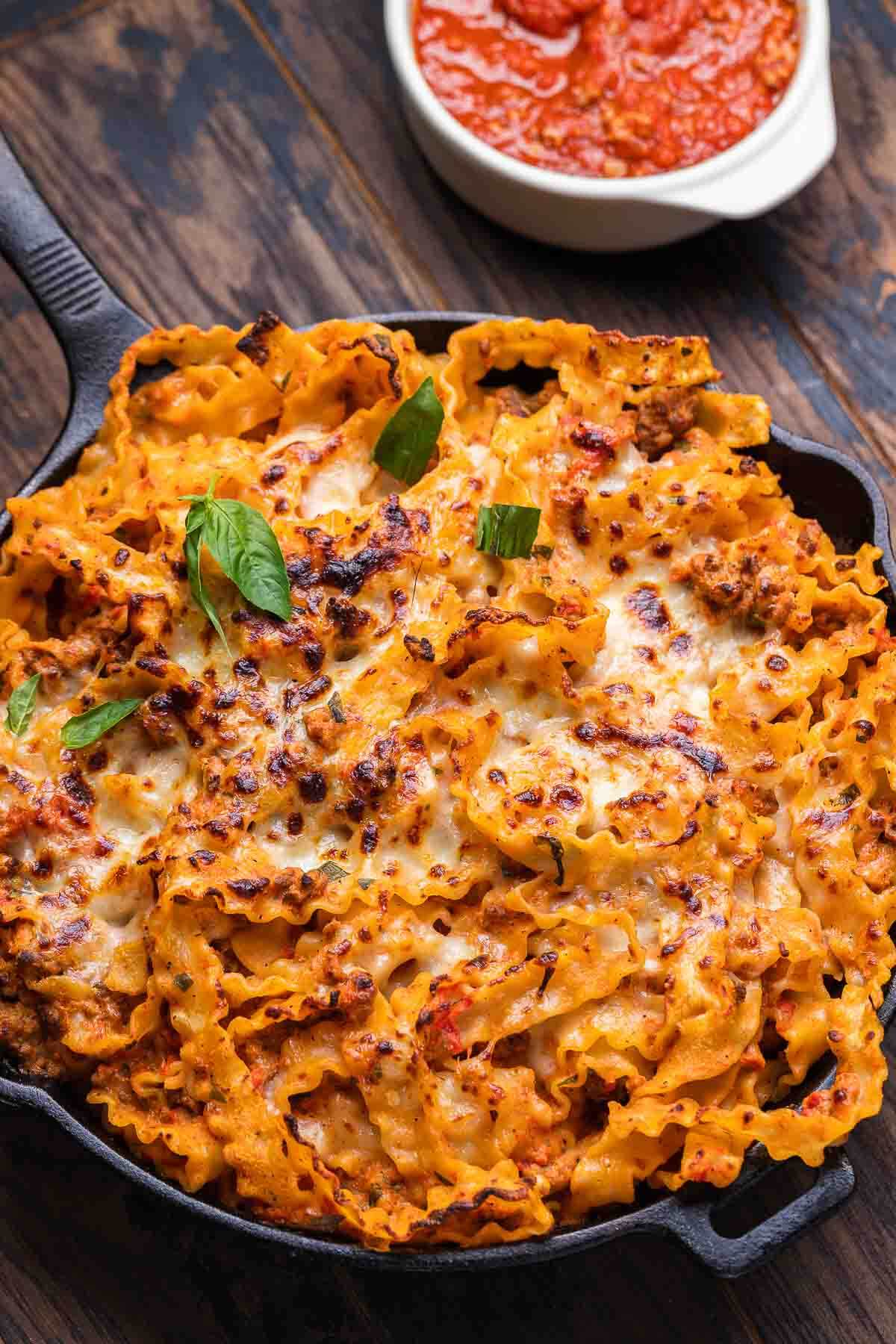 Overhead shot of baked lasagna pie with a bowl of sauce in the background.