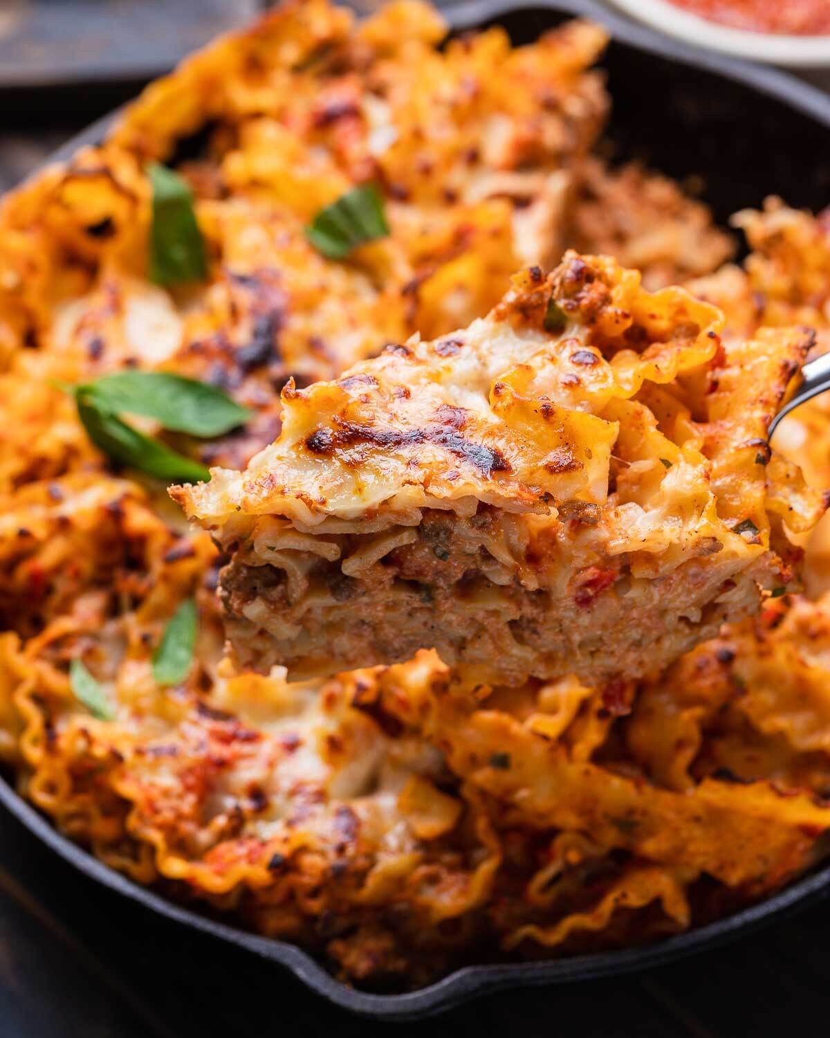 Cake server holding a slice of lasagna pie over cast iron pan.