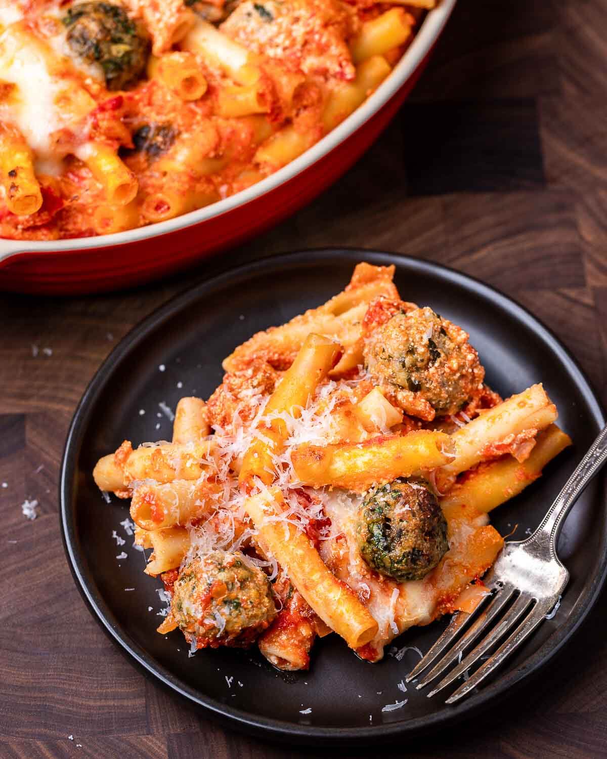 Black plate with baked ziti with meatballs.