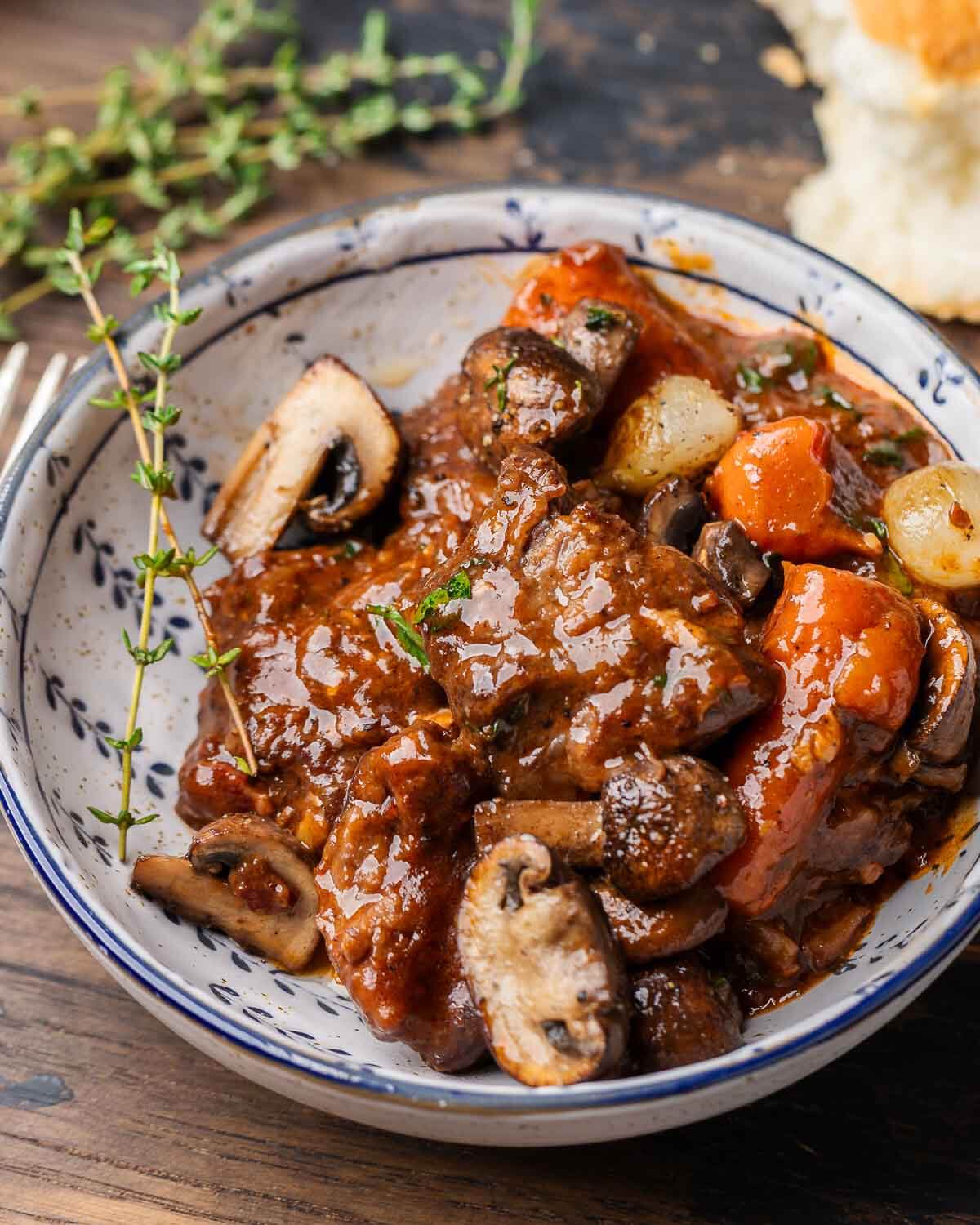 Beef Bourguignon in white bowl with thyme garnish.