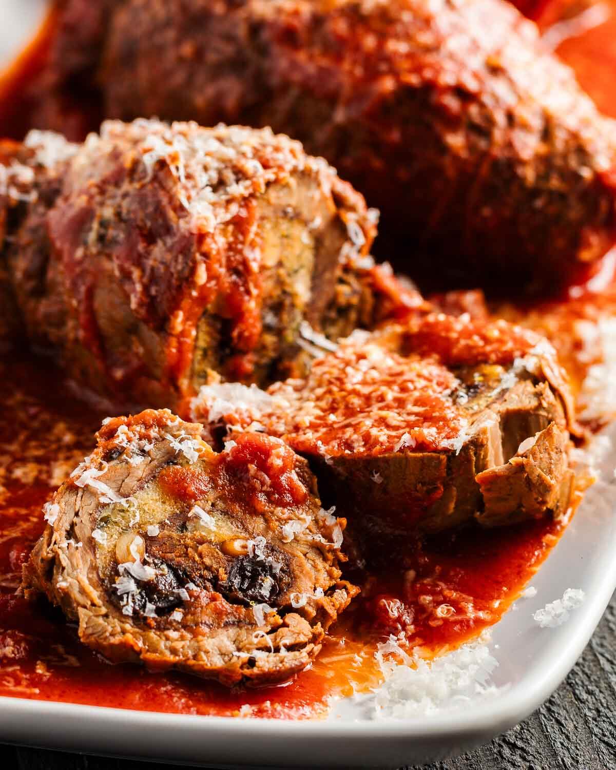 Beef braciole cut open and showing interior in white plate.