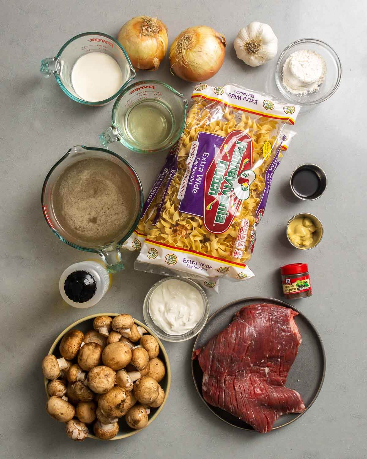 Ingredients shown: cream, wine, onion, garlic, flour, egg noodles, beef stock, sour cream, mushrooms, olive oil, flank steak, mustard, spices, and worcestershire sauce.