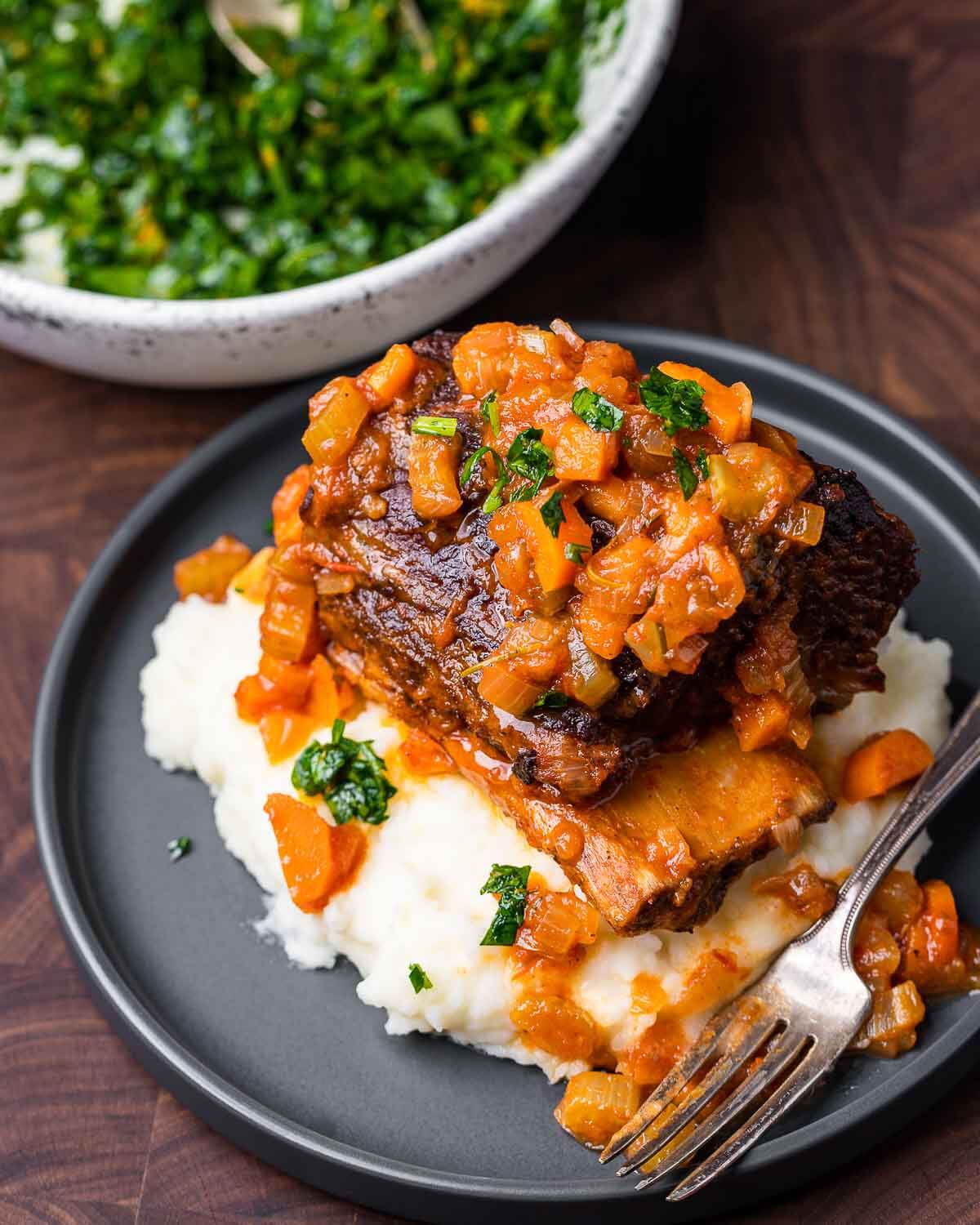 Braised short rib on top of mashed potatoes in grey plate.