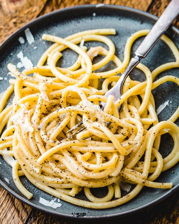 Plate of cacio e pepe with grated Pecorino Romano on top of wood table.