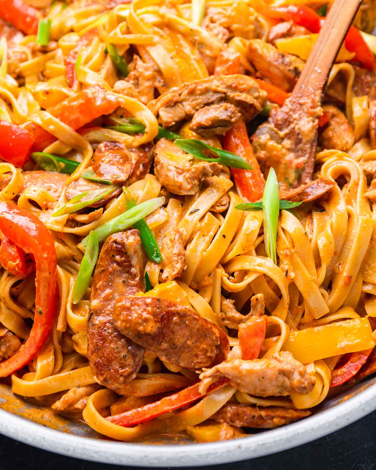 Cajun fettuccine pasta in pan with Andouille sausage pieces in the front of pic.