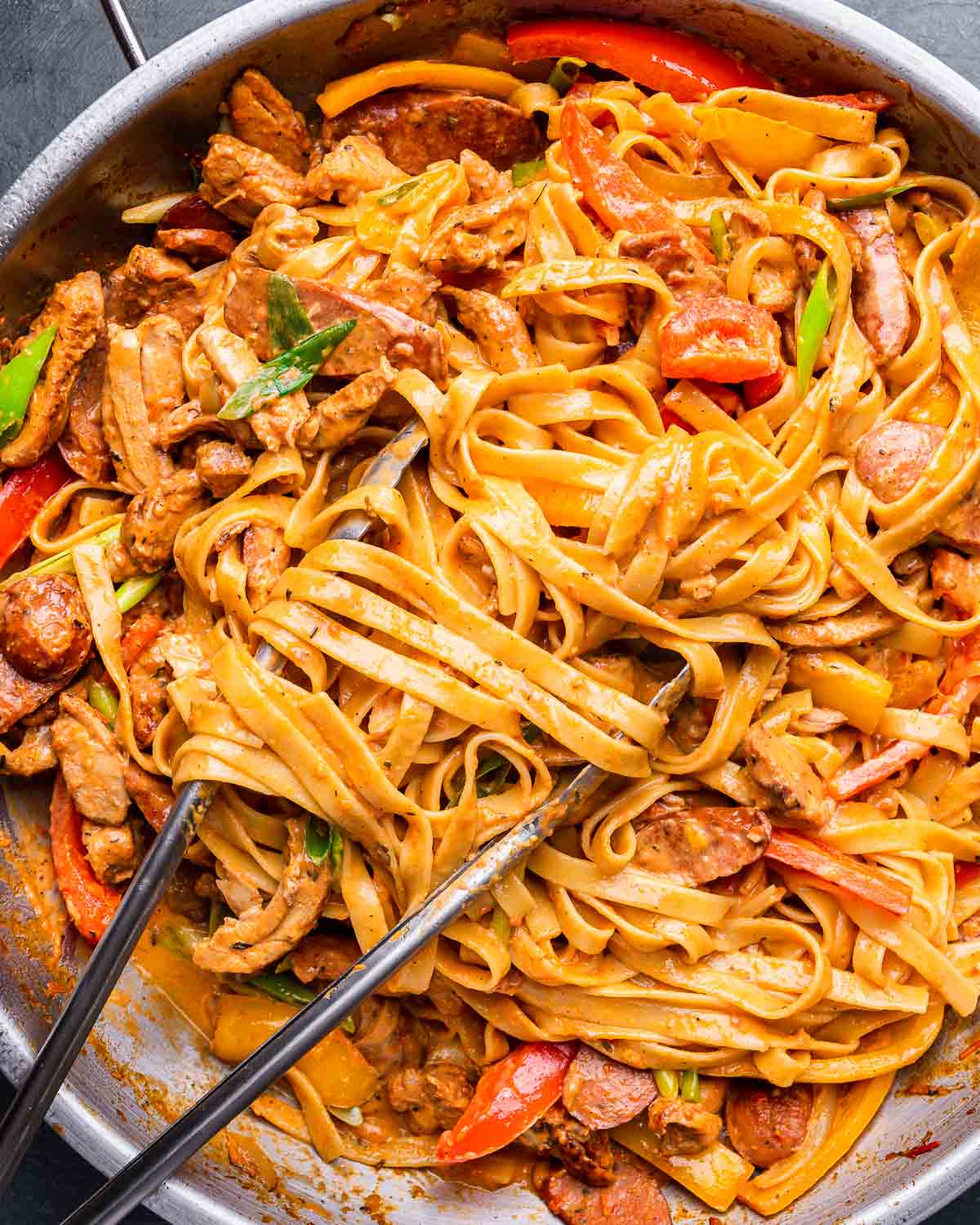 Cajun chicken pasta in large pan with metal tongs.