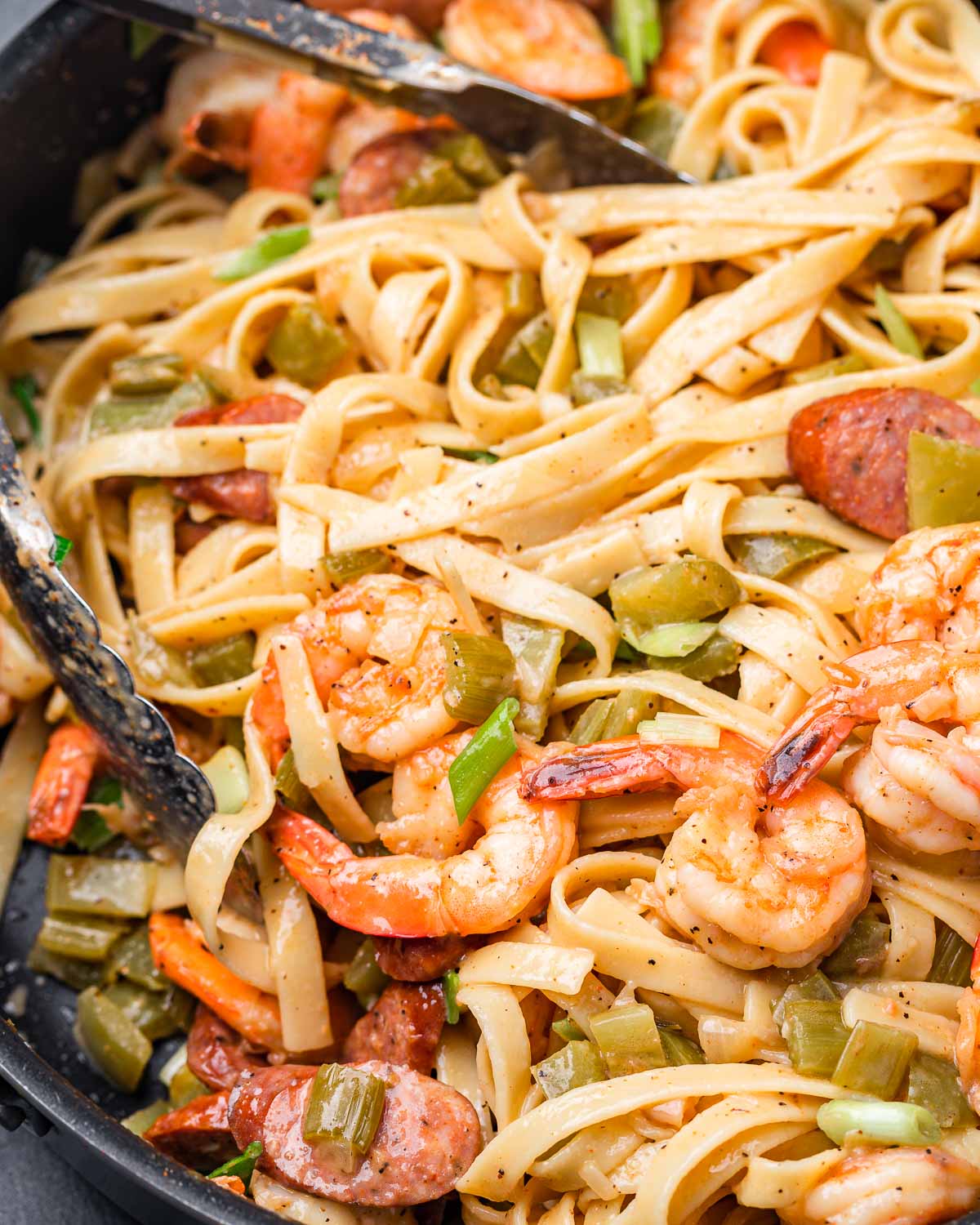 Cajun shrimp and sausage pasta in large pan with tongs.