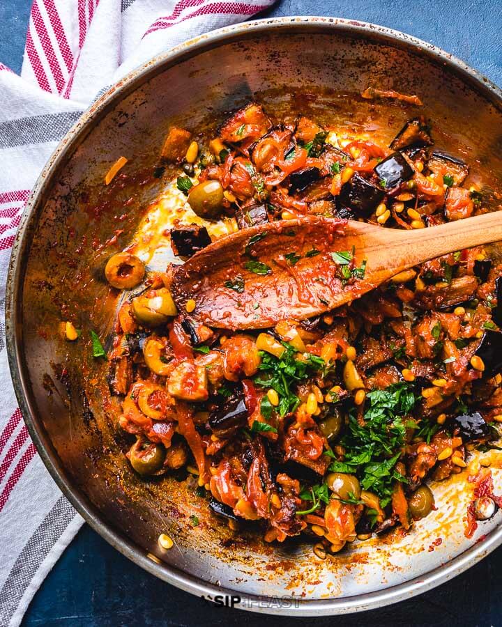 Pan of caponata with large wooden spoon.