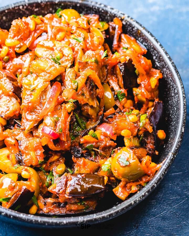 Eggplant caponata in black bowl on blue board.