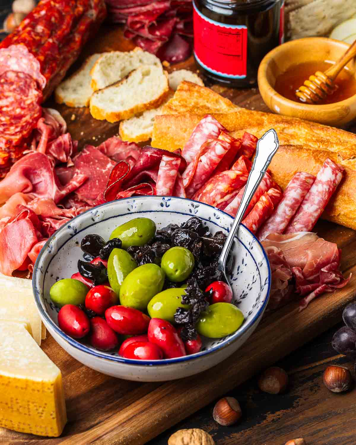 Charcuterie board with plate of olives in center.