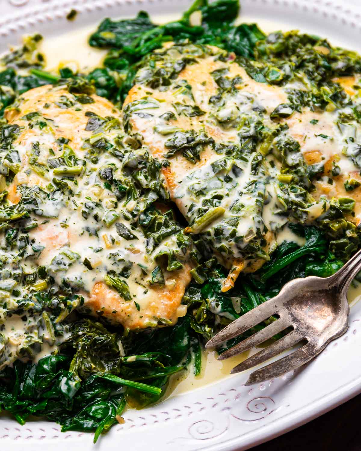 Chicken Florentine on bed of spinach in white platter.