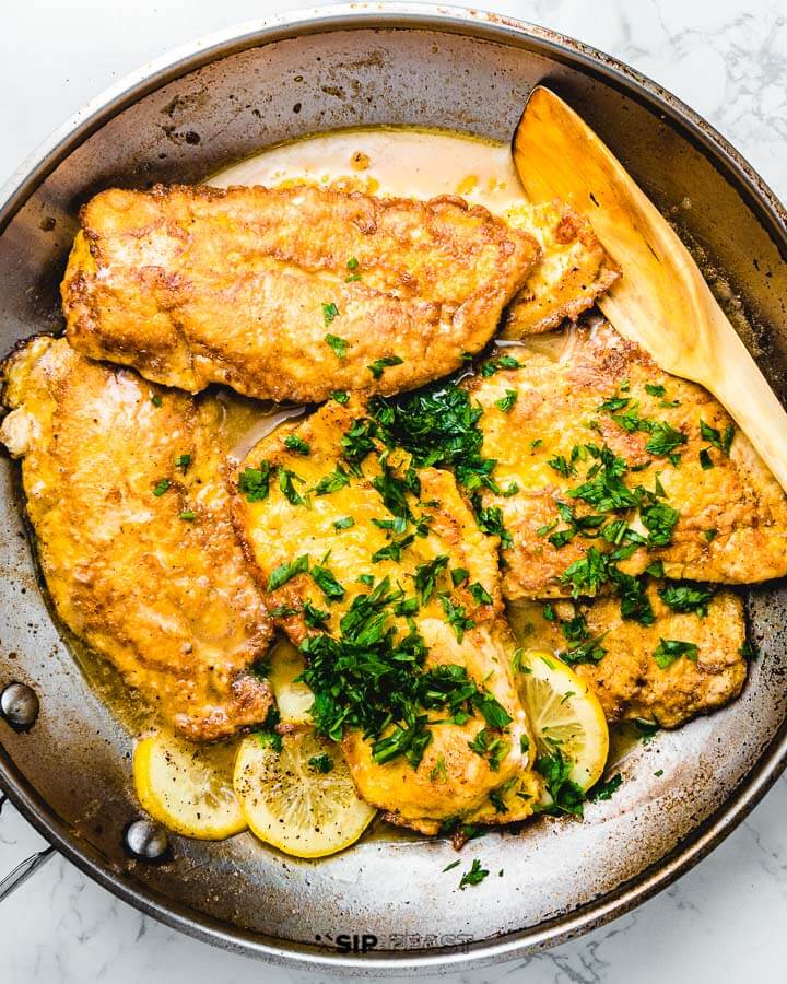 Chicken Francese in large pan with parsley sprinkled on top.