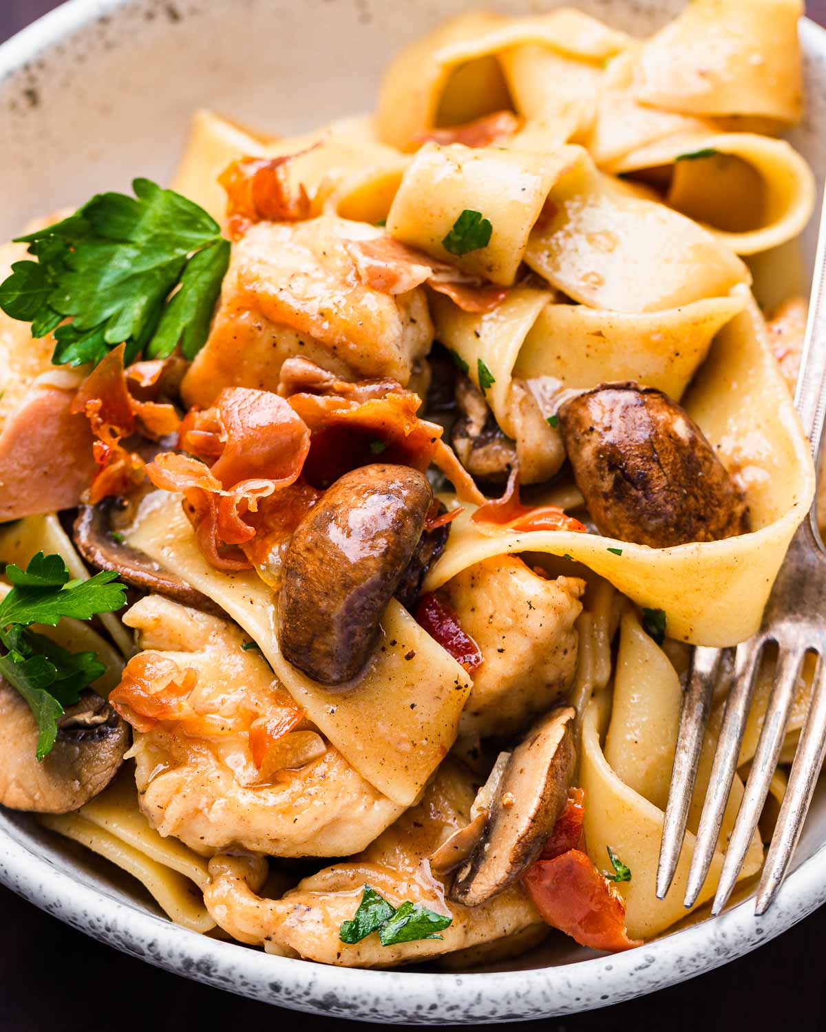 Chicken marsala pappardelle pasta in white bowl with fork.