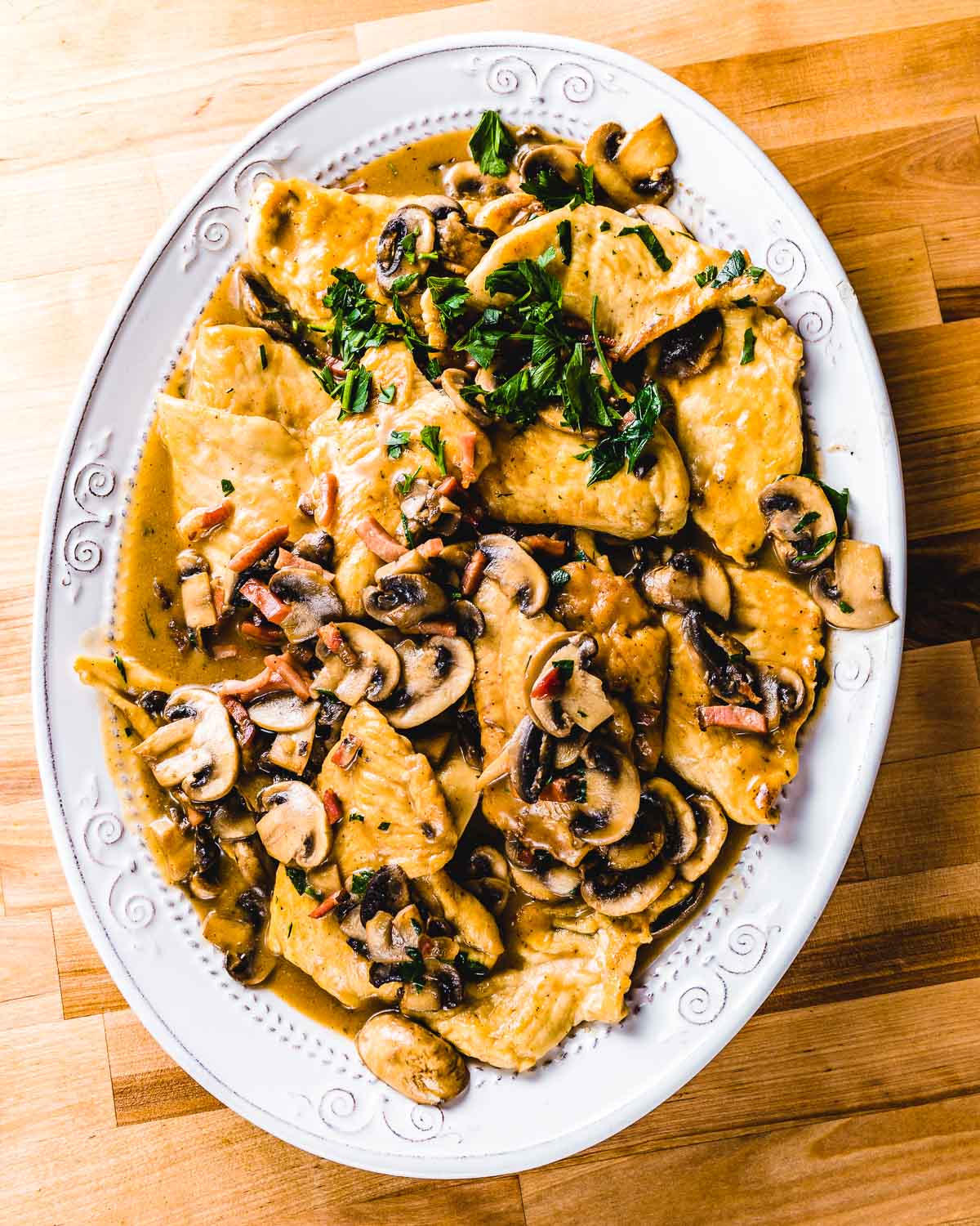 Large white plate of chicken marsala on wood table.