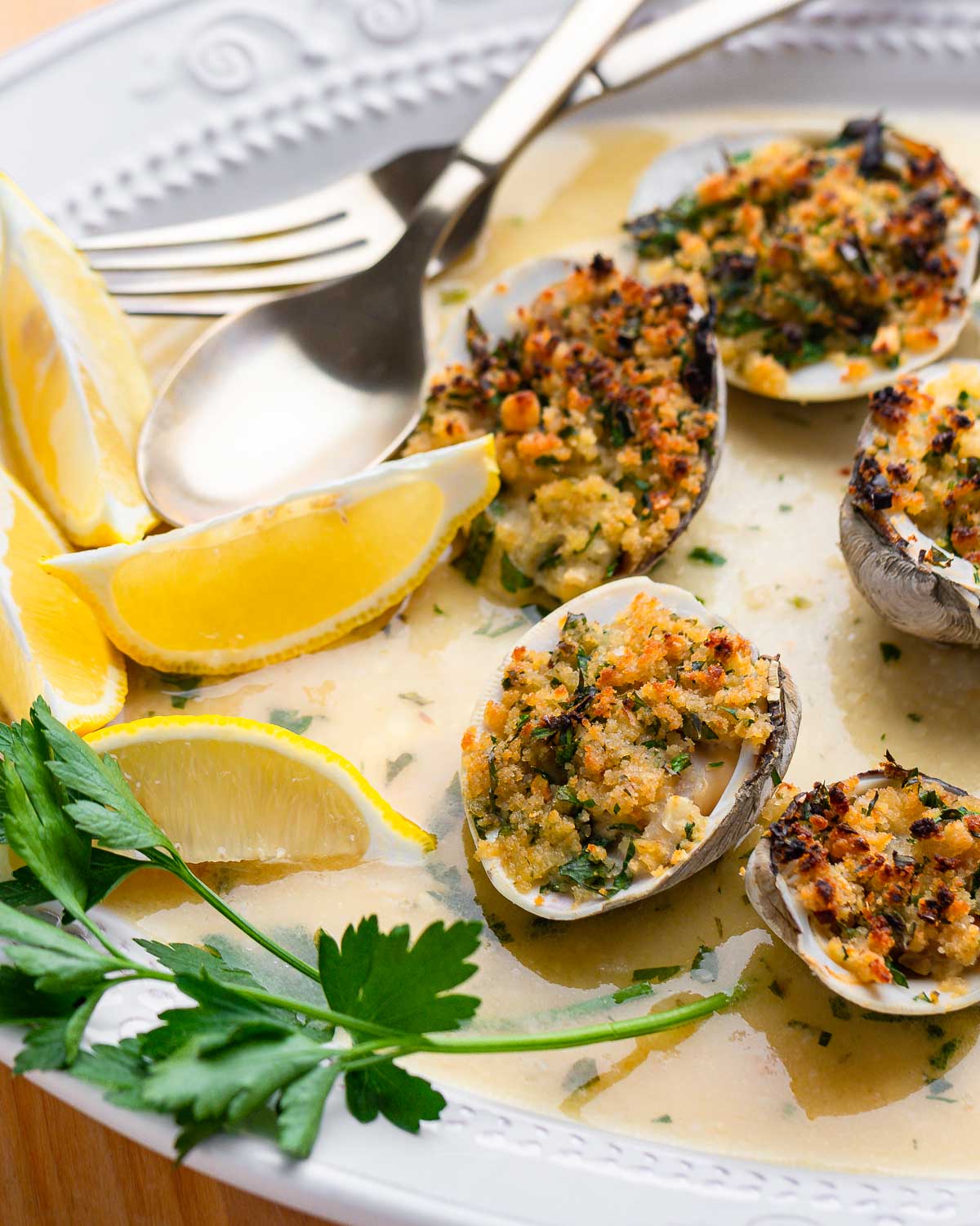 Clams oreganata in white dish with lemon wedges and parsley garnish.