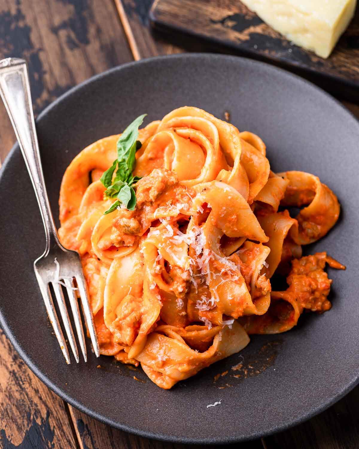 Grey plate with creamy Italian sausage pasta and grated cheese.