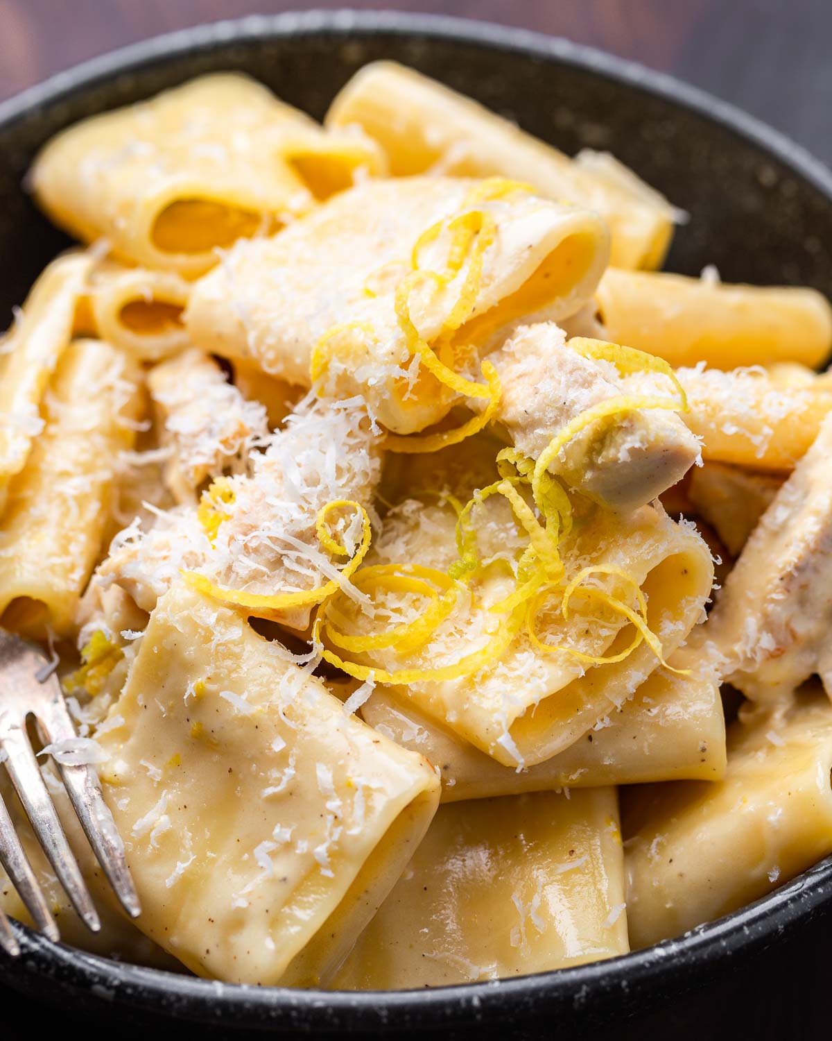 Creamy lemon chicken pasta in black bowl with lemon zest and cheese on top.