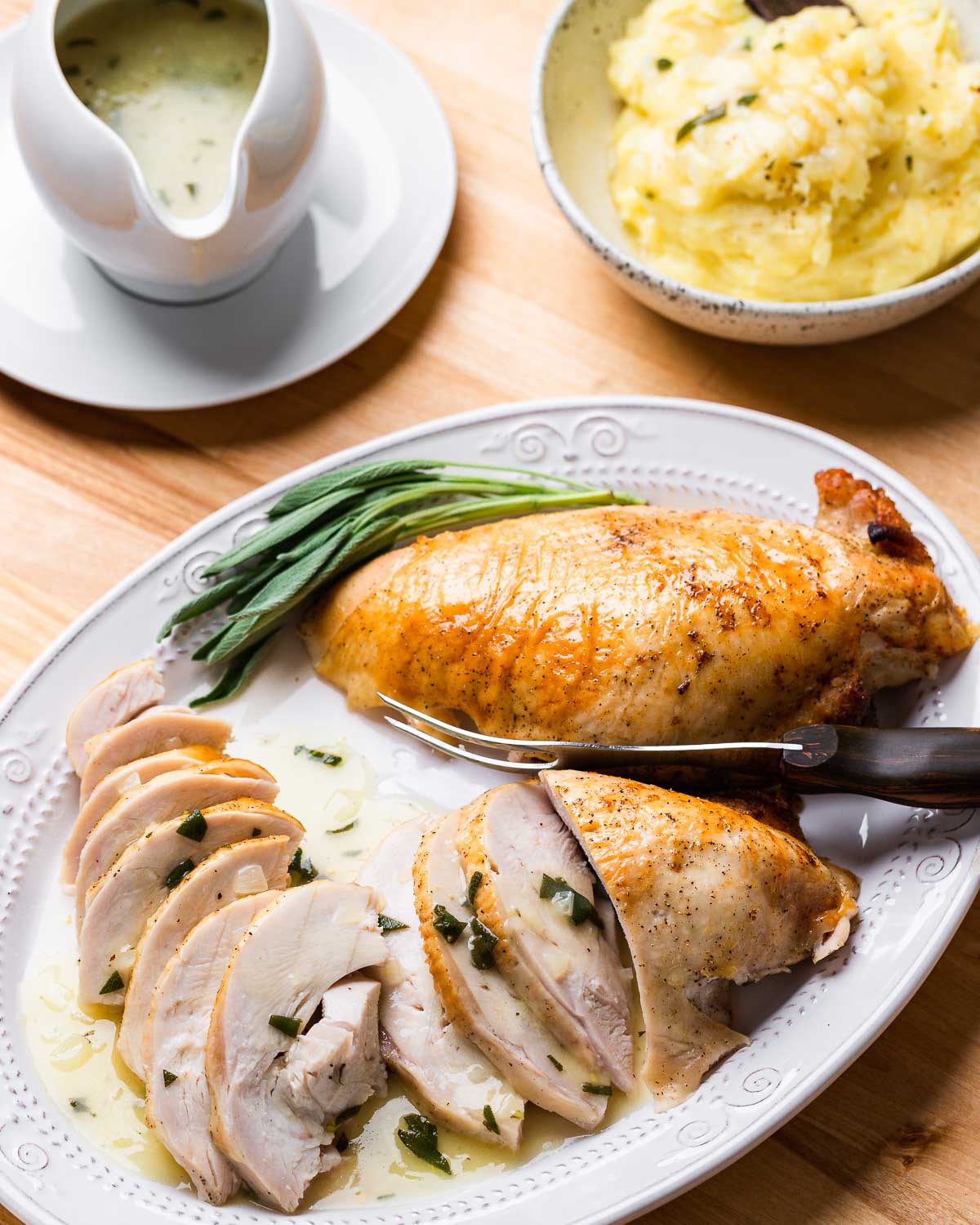 Platter with carved turkey breast, bowl of mashed potatoes, and gravy boat.