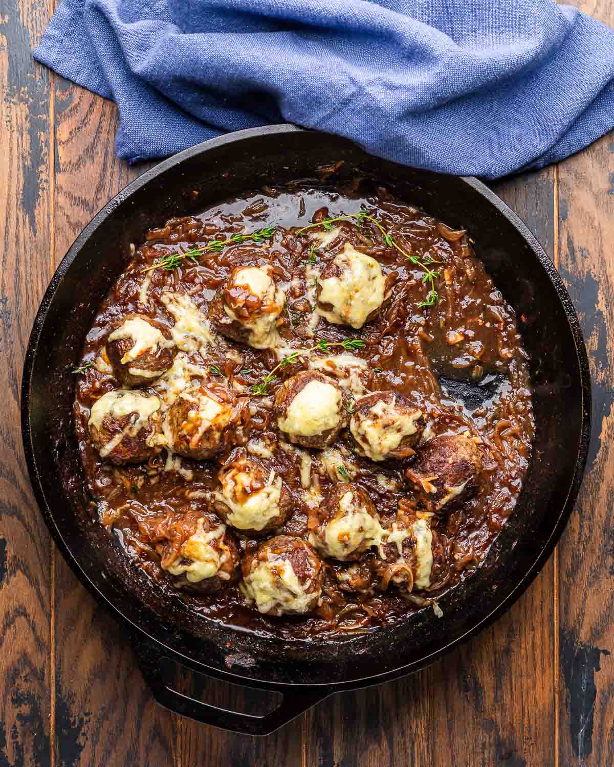 French onion meatballs in cast iron pan with blue napkin.