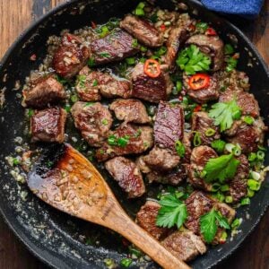 Garlic butter steak bites in black pan with wooden spoon.