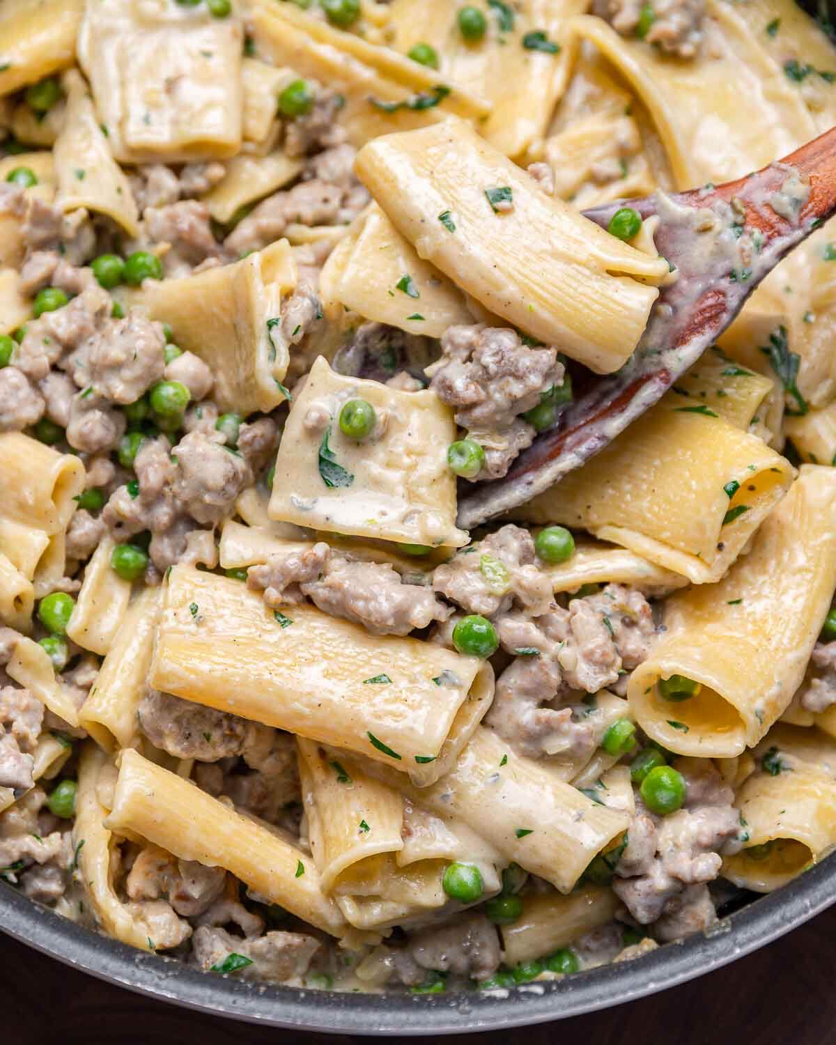 Wooden spoon scooping out gorgonzola cream sauce pasta from large pan.