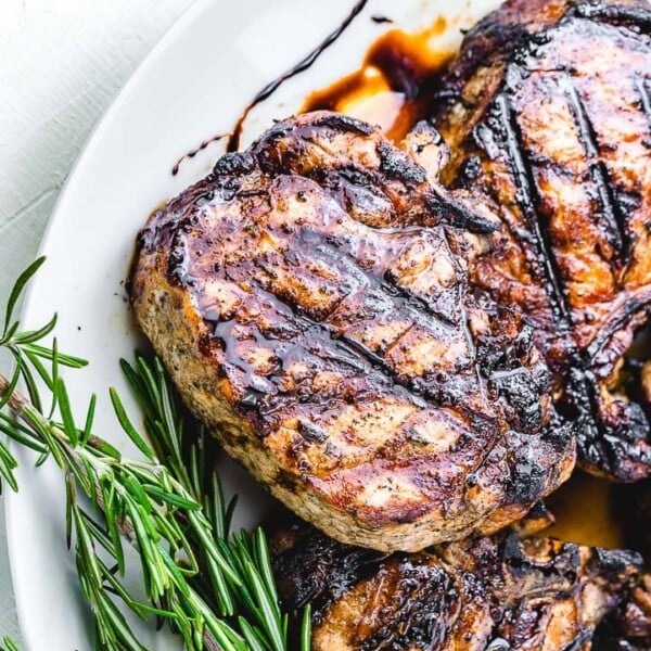 Grilled pork chop with balsamic glaze and rosemary garnish in white plate.