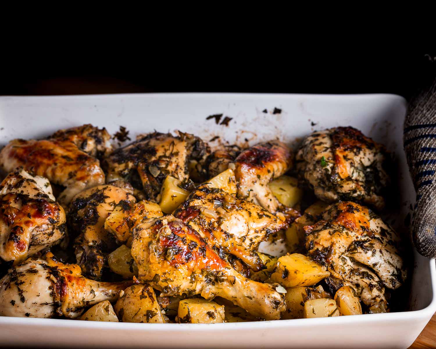 Italian baked chicken and potatoes being held in white baking dish.