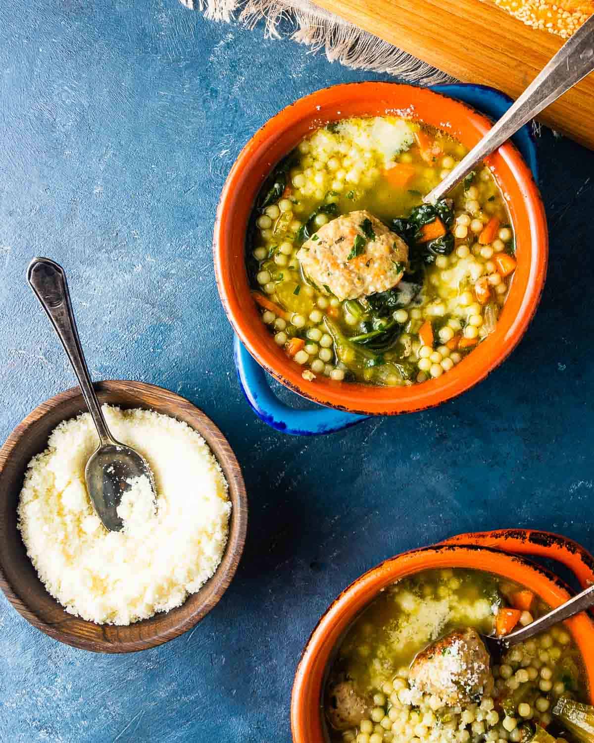 Two bowls of soup and one bowl of grated cheese on blue board.