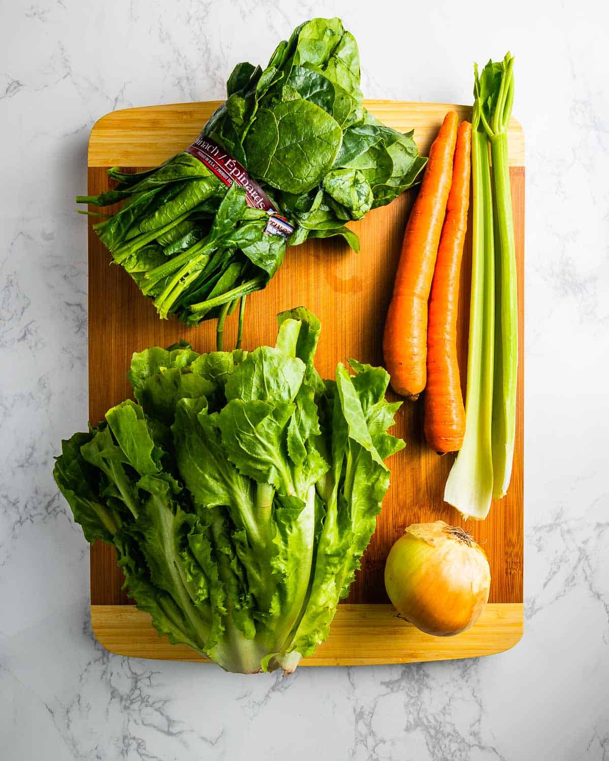 Escarole, spinach, carrots, onion, and celery on cutting board.