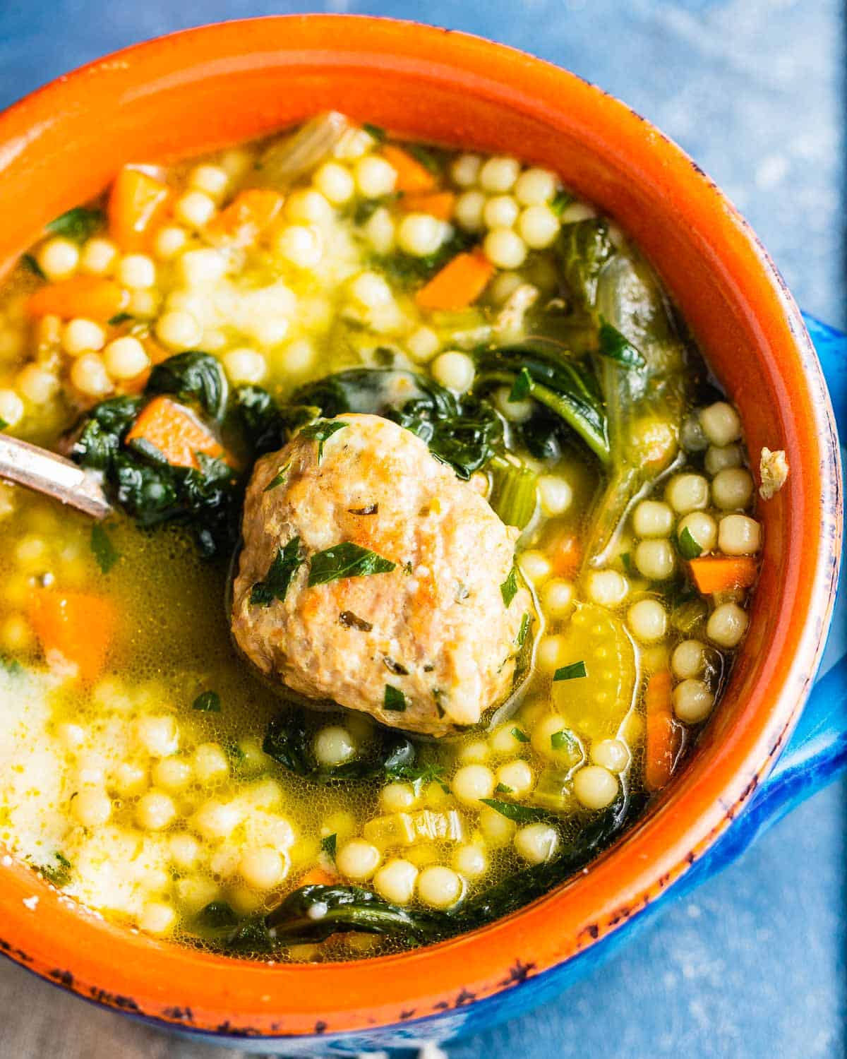 Bowl of Italian wedding soup with a turkey meatball on spoon.