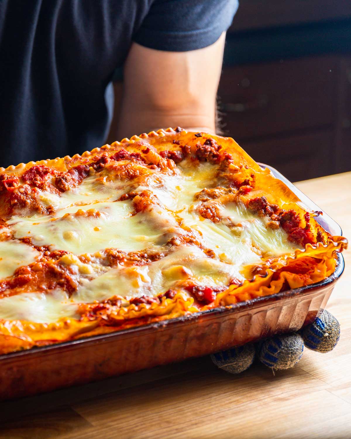 Lasagna in glass baking dish being held over table.