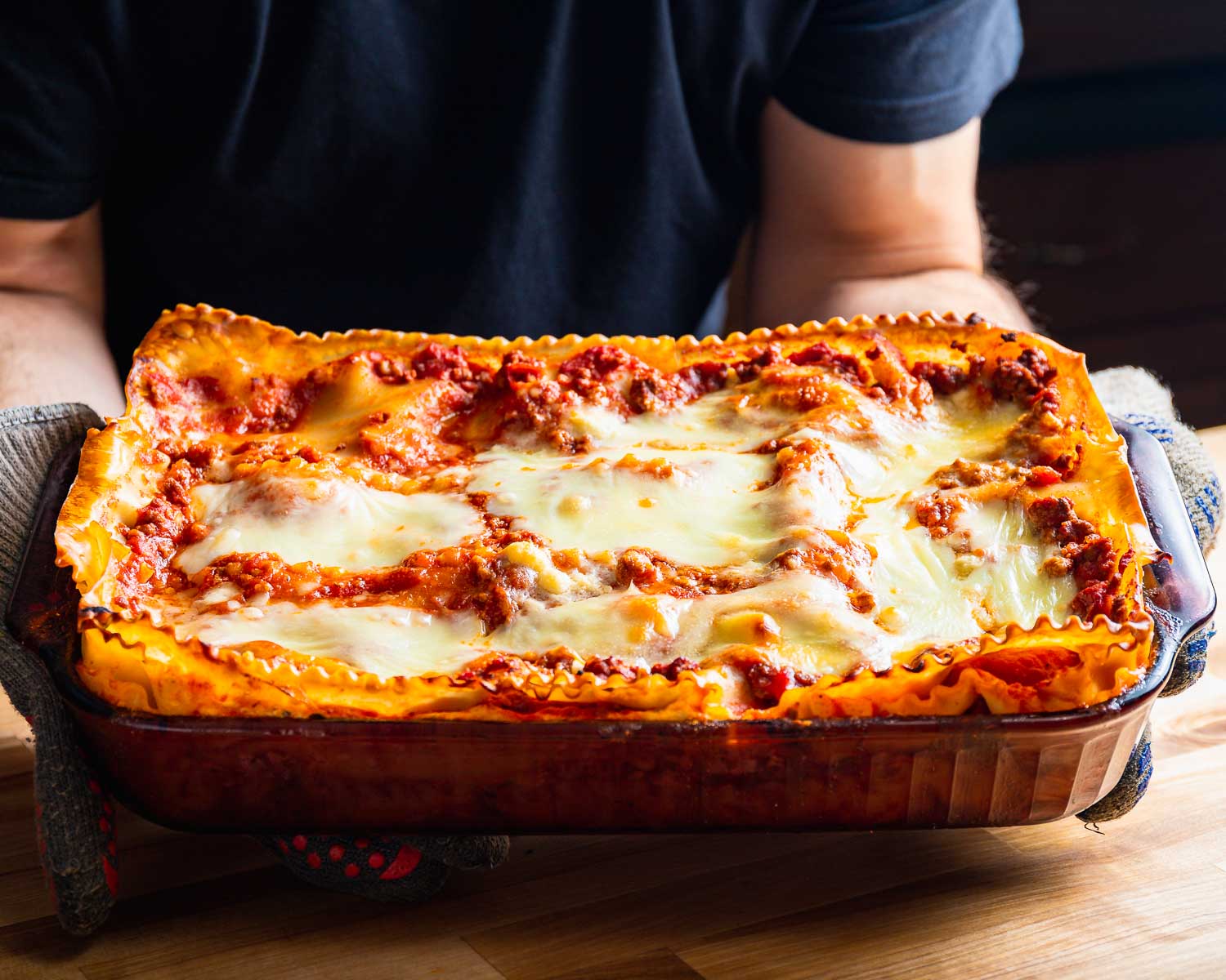 Tray of lasagna being held with gloves.