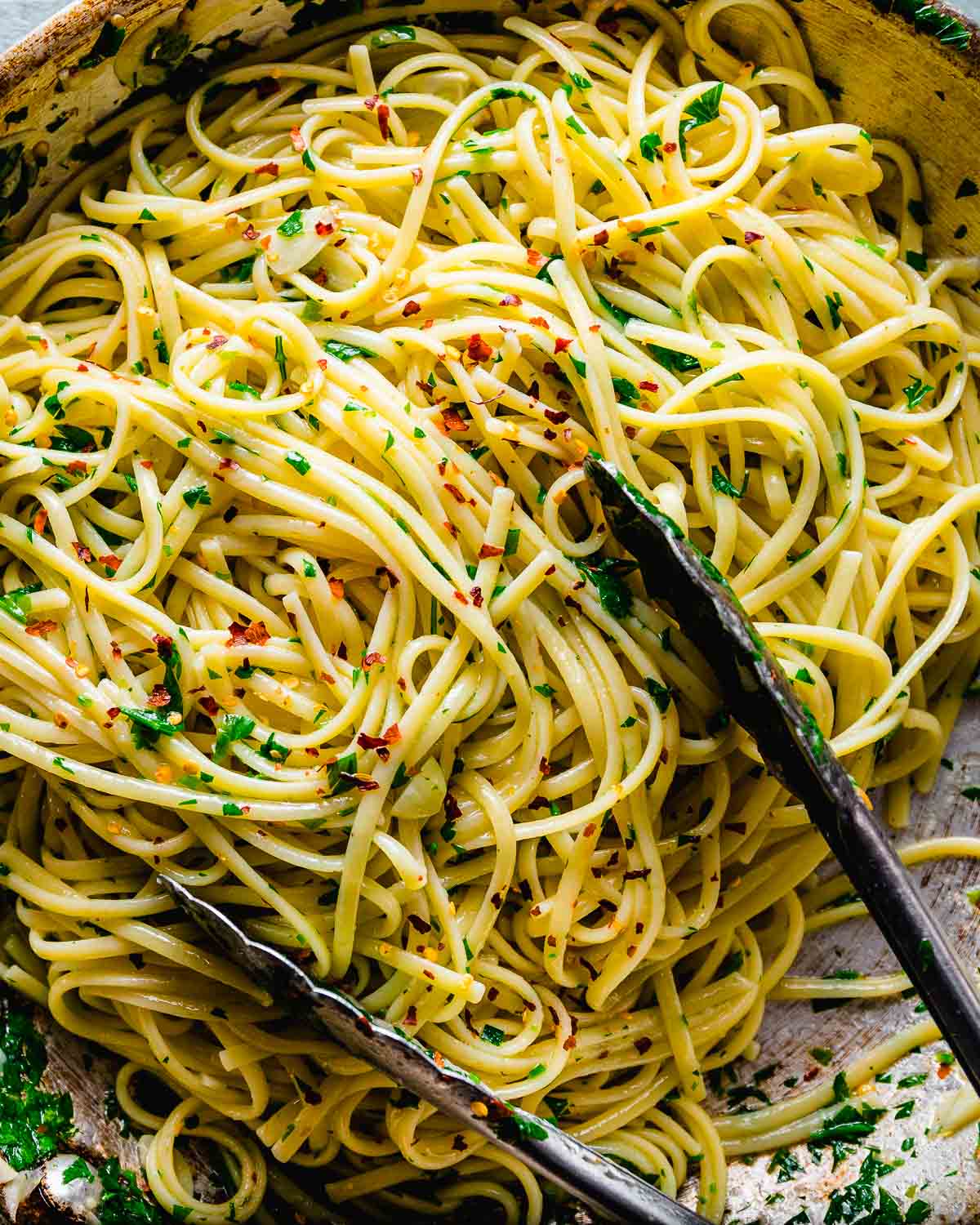 Linguine with garlic and oil in pan with tongs.