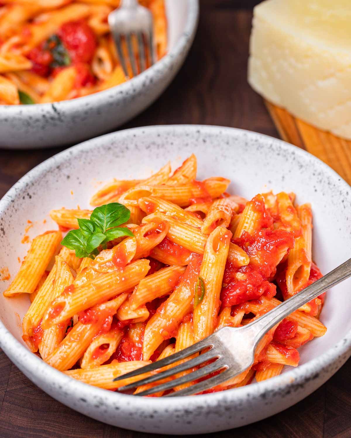 Bowl of penne with marinara sauce and cheese in the background.