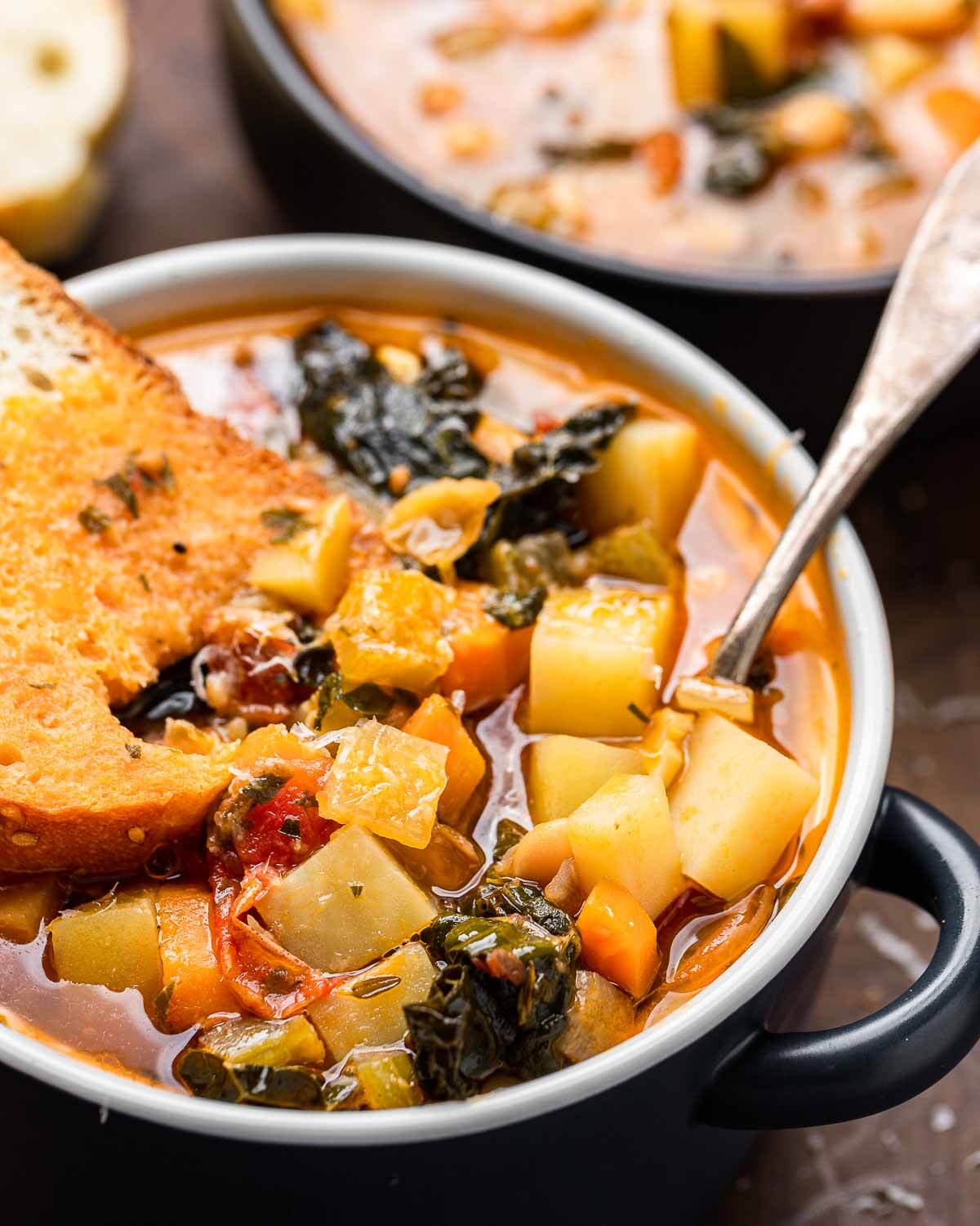 Small bowl of minestrone soup with bread dipped into it.