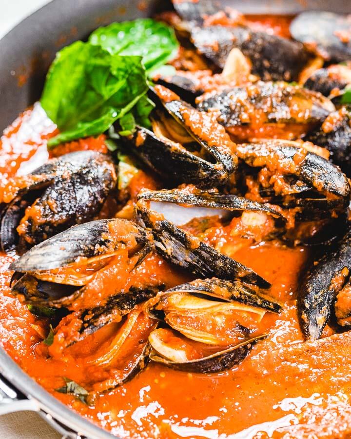 Pan with mussels in the marinara sauce with basil in background.