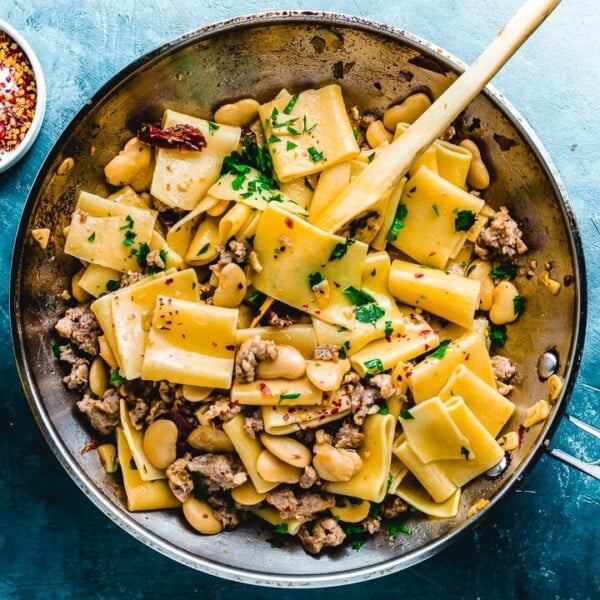 Paccheri pasta with butter beans in pan on blue background.