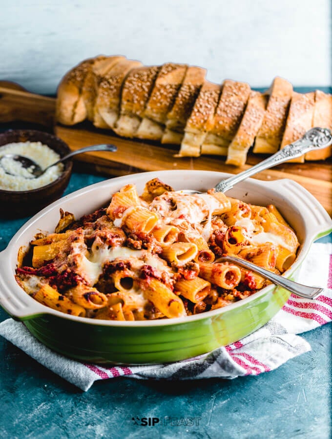 Pasta al forno on table with bread and grated cheese.