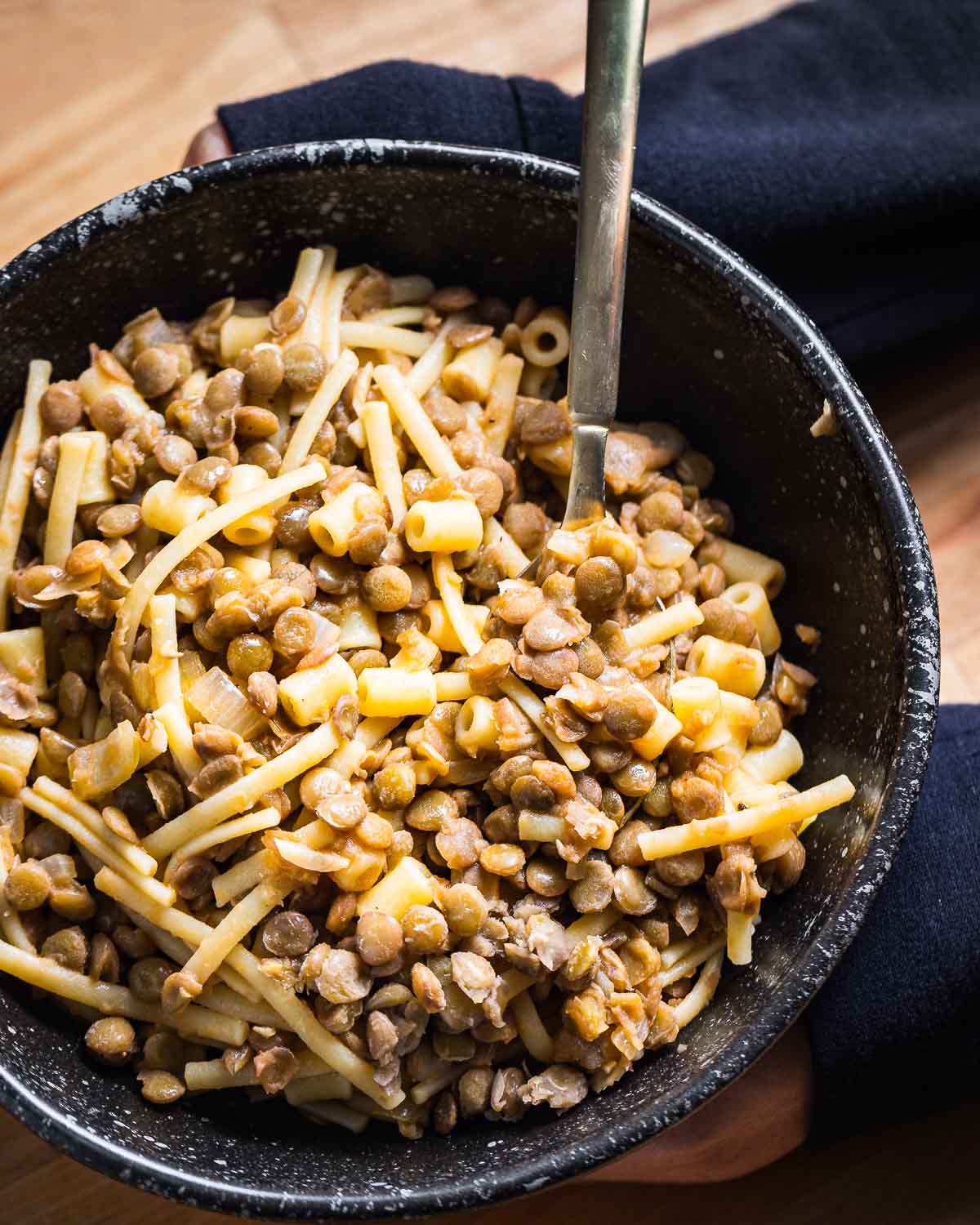 Black bowl of pasta with lentils held in hands.