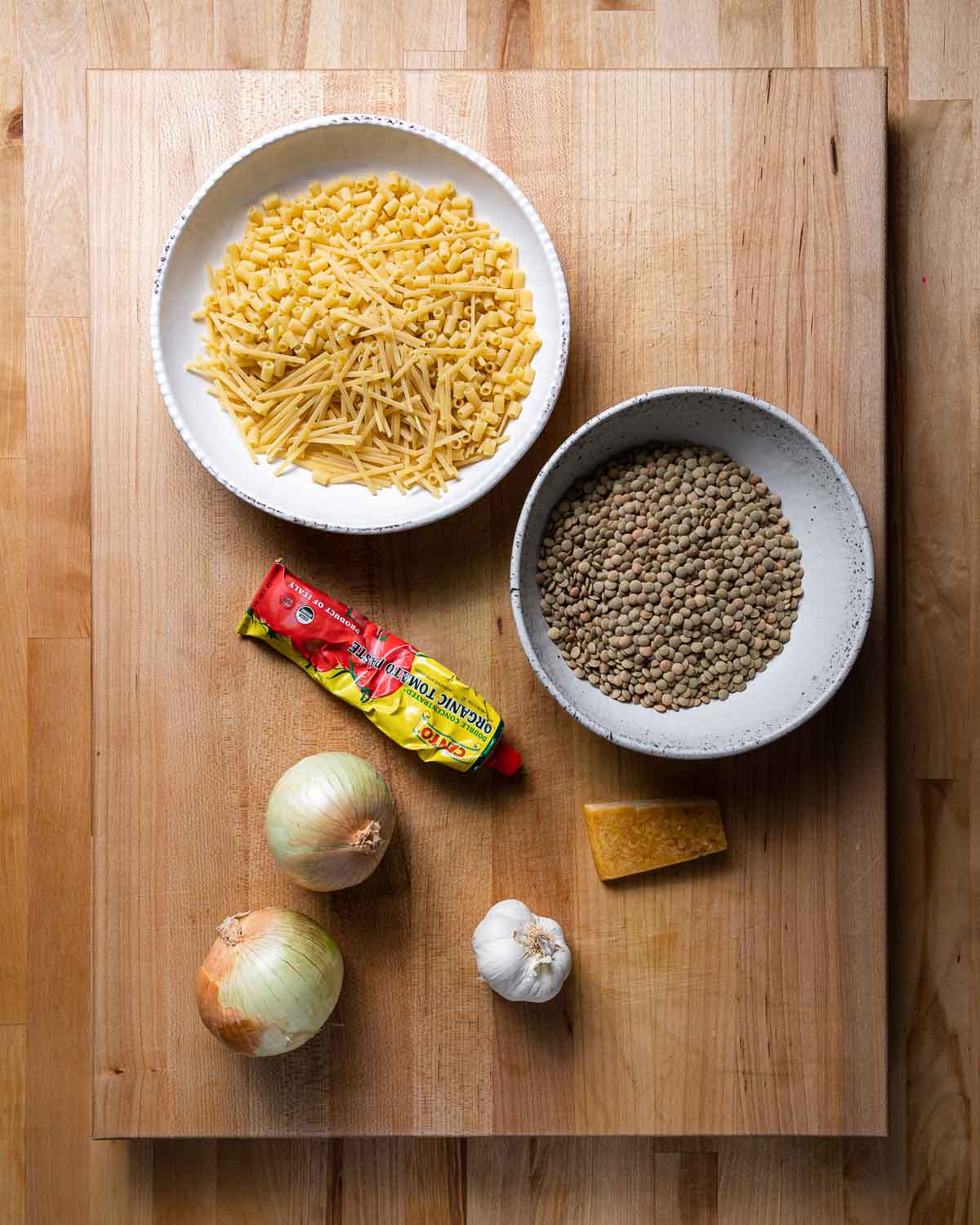 Ingredients shown: bowl of broken spaghetti and various pasta, lentils, tomato paste, onions, garlic, and parmesan rind.