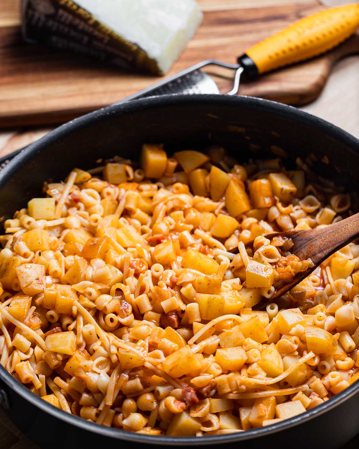 Pasta e patate in large black pan with block of Pecorino in background.