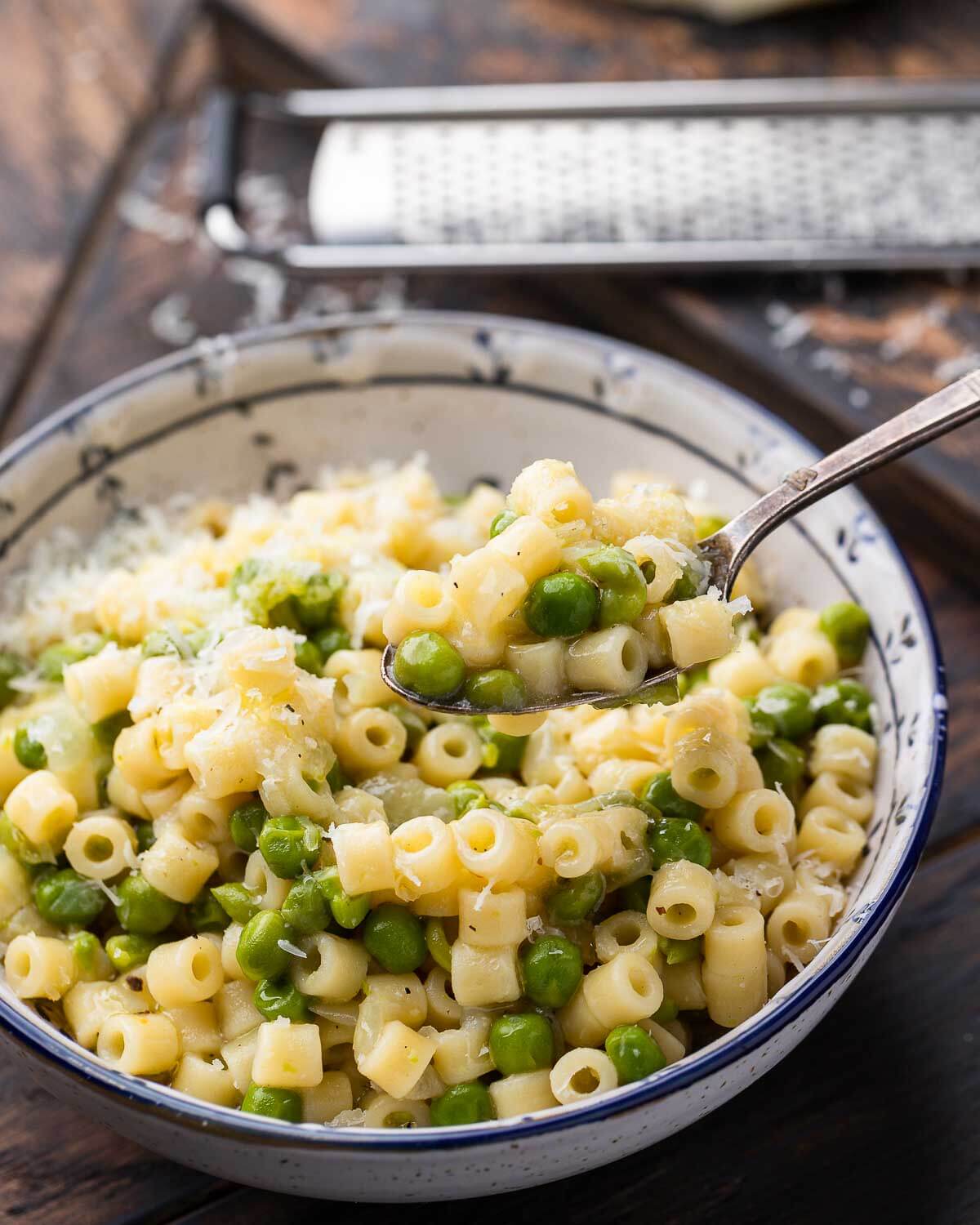 Bowl of pasta e piselli with spoonful held above the bowl.