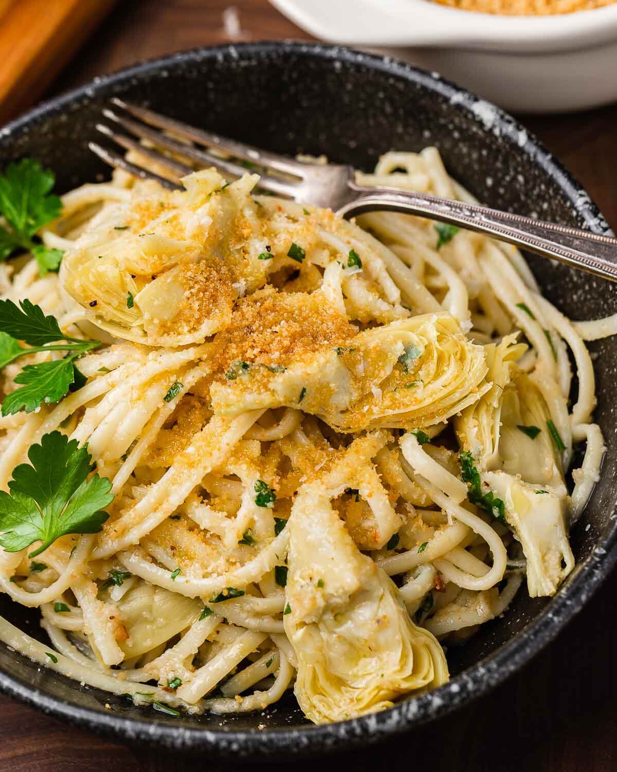 Black plate with linguine, artichoke hearts, and breadcrumbs.