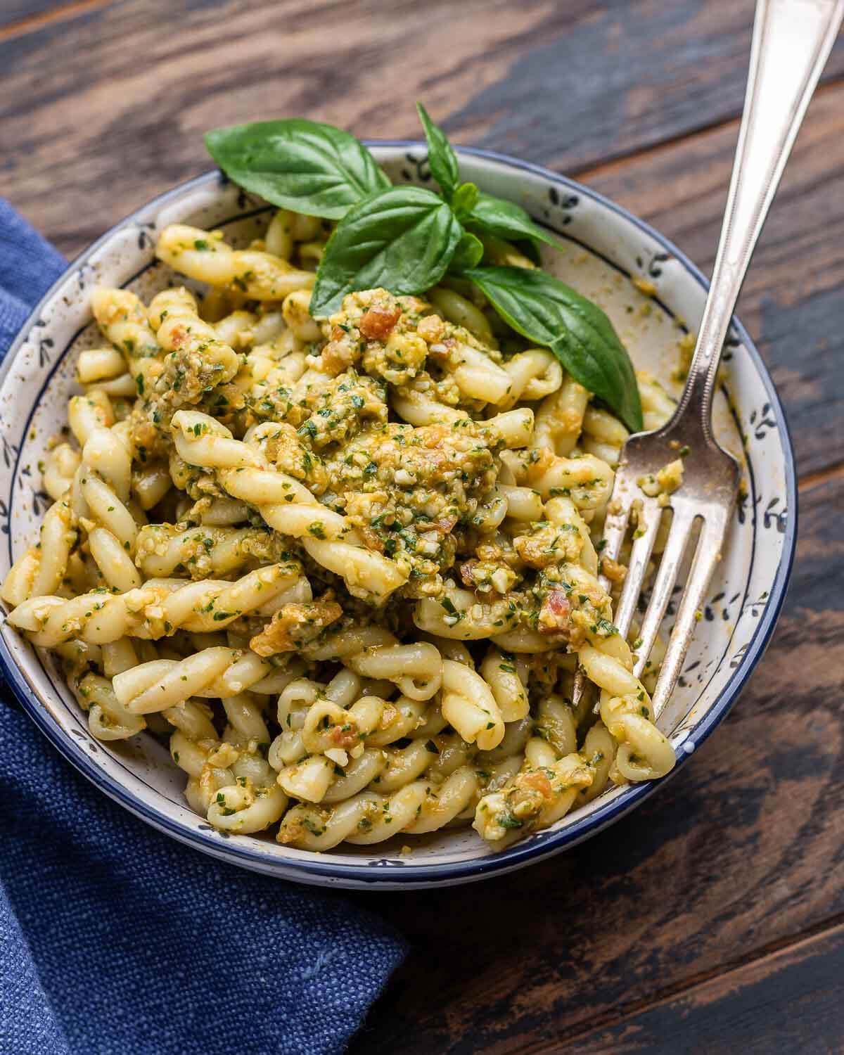 Small white and blue bowl of pasta with pesto alla Trapanese and basil garnish.