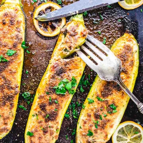 Ricotta stuffed zucchini boats in pan with fork and knife.